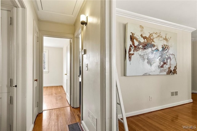 corridor featuring baseboards, wood finished floors, visible vents, and crown molding