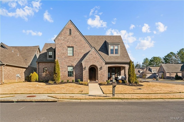 english style home featuring brick siding, roof with shingles, and a residential view