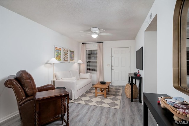 living area featuring a ceiling fan, a textured ceiling, and light wood finished floors