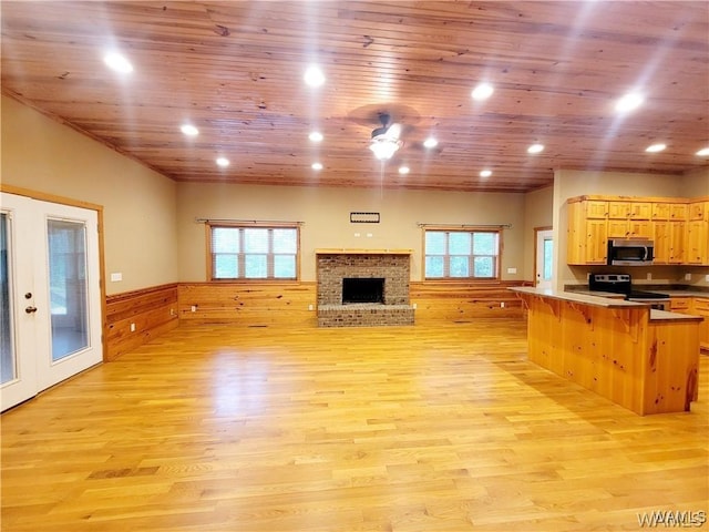 unfurnished living room with a brick fireplace, wood ceiling, light wood-style floors, and wainscoting