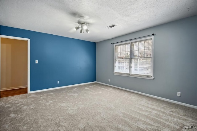 spare room with a textured ceiling, carpet flooring, a ceiling fan, visible vents, and baseboards