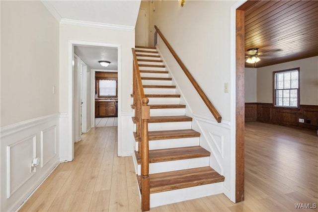 stairs featuring ceiling fan, a wainscoted wall, crown molding, and wood finished floors