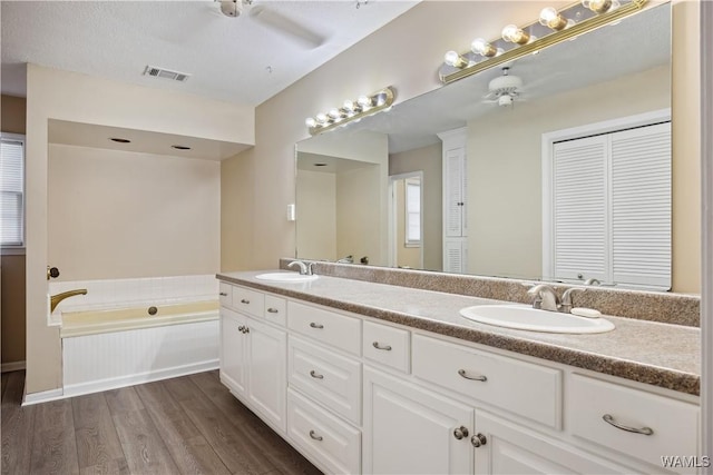 full bath featuring a garden tub, visible vents, a sink, and wood finished floors