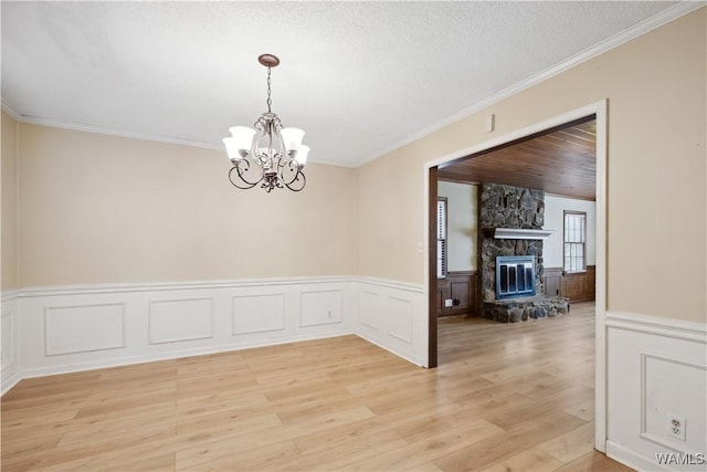 unfurnished dining area with a textured ceiling, a stone fireplace, light wood-type flooring, and crown molding