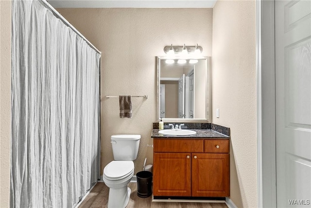 bathroom with a textured wall, toilet, wood finished floors, vanity, and a shower with curtain