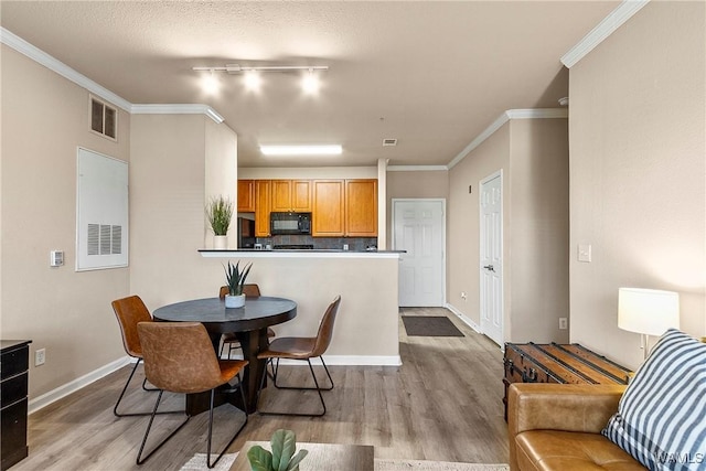 dining space with light wood-style floors, visible vents, crown molding, and baseboards