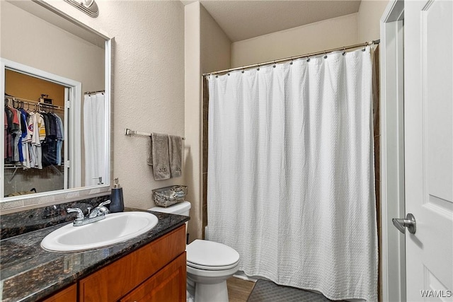 bathroom featuring a walk in closet, a textured wall, vanity, and toilet