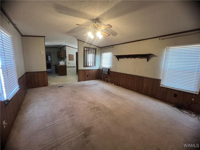 unfurnished living room with crown molding, vaulted ceiling, ceiling fan, a textured ceiling, and light colored carpet