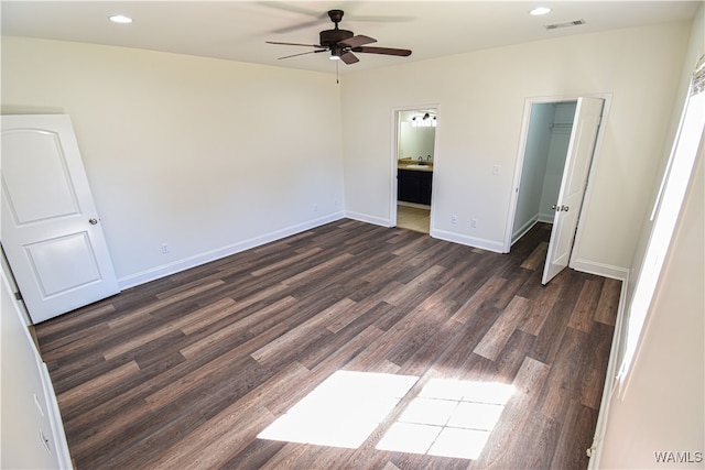 unfurnished bedroom featuring a walk in closet, dark hardwood / wood-style floors, ensuite bath, and ceiling fan