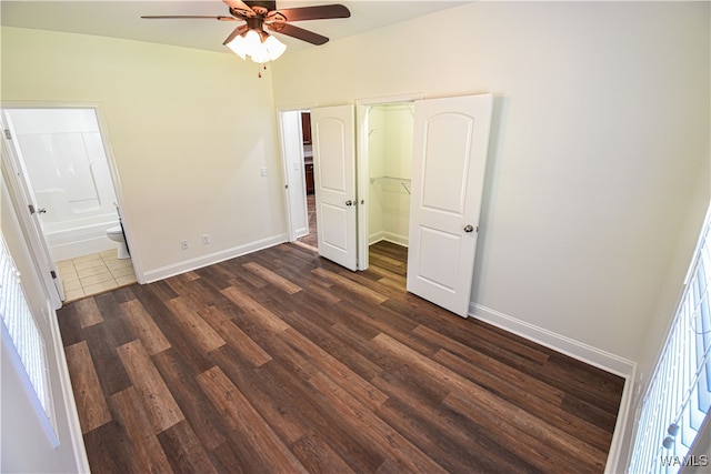 unfurnished bedroom featuring multiple windows, dark hardwood / wood-style floors, ensuite bath, and ceiling fan