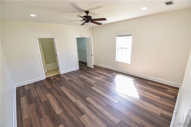 unfurnished bedroom with a walk in closet, connected bathroom, ceiling fan, and dark wood-type flooring