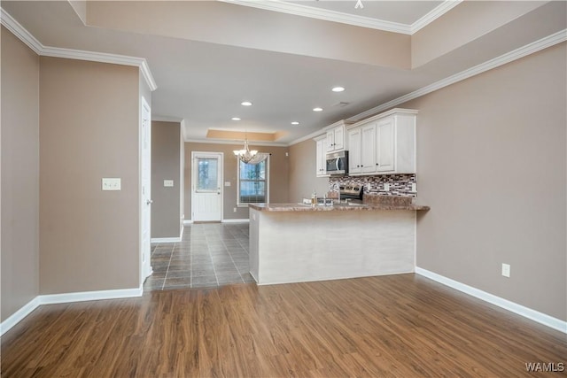 kitchen with stainless steel appliances, kitchen peninsula, white cabinets, decorative backsplash, and a raised ceiling