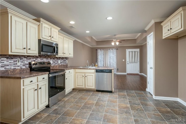 kitchen featuring sink, stainless steel appliances, cream cabinets, ornamental molding, and a raised ceiling