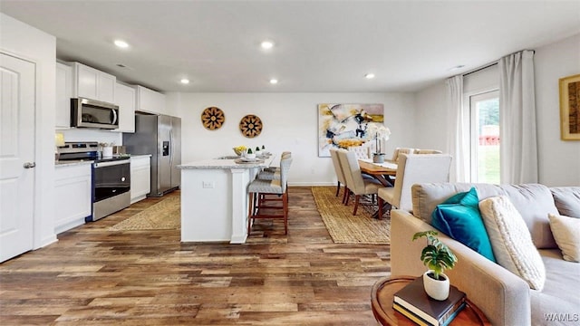 kitchen with a breakfast bar, wood finished floors, stainless steel appliances, white cabinetry, and recessed lighting