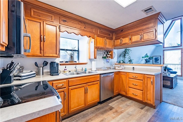 kitchen with sink, light wood-type flooring, kitchen peninsula, and appliances with stainless steel finishes