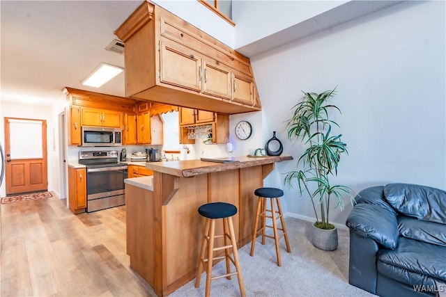 kitchen with stainless steel appliances, a breakfast bar, kitchen peninsula, and light wood-type flooring