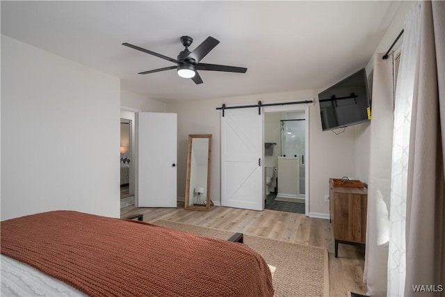 bedroom with hardwood / wood-style flooring, ensuite bathroom, a barn door, and ceiling fan