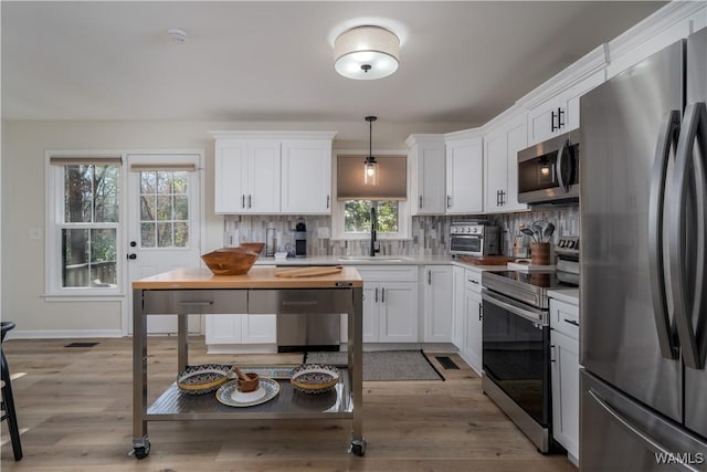 kitchen with stainless steel appliances, sink, pendant lighting, light hardwood / wood-style flooring, and white cabinets