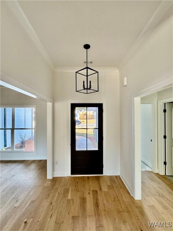 foyer with crown molding, a notable chandelier, and light wood-type flooring