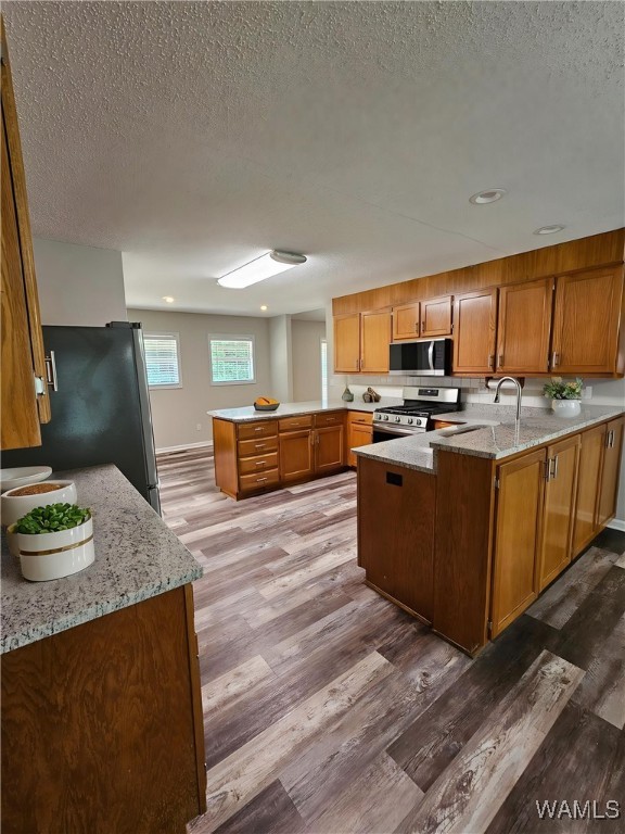 14541 Keenes Mill Rd, Coaling, AL 35453 - kitchen with stainless steel appliances, a peninsula, light wood finished floors, light stone countertops, and a textured ceiling