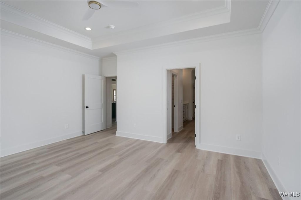 unfurnished room with a tray ceiling, light wood-style flooring, baseboards, and ornamental molding