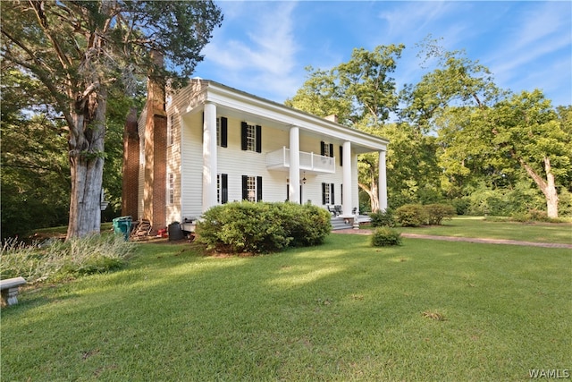 greek revival inspired property with a balcony and a front yard