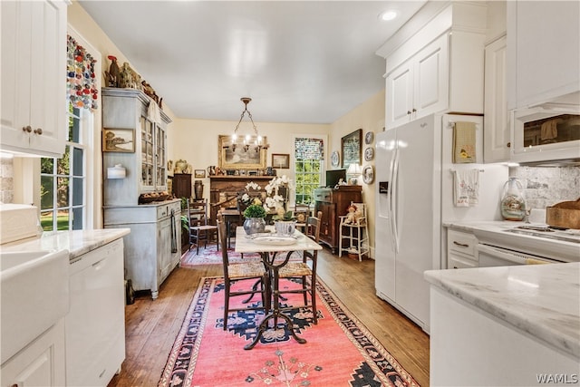 kitchen with light stone counters, white appliances, wood-type flooring, decorative light fixtures, and white cabinets