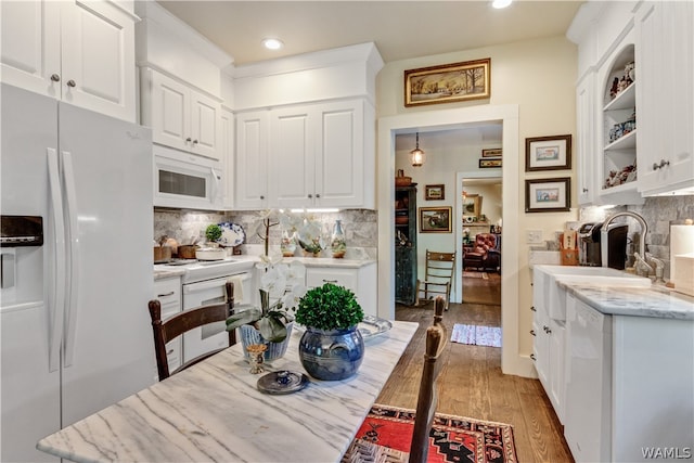 kitchen with white appliances, sink, hardwood / wood-style flooring, light stone counters, and white cabinetry