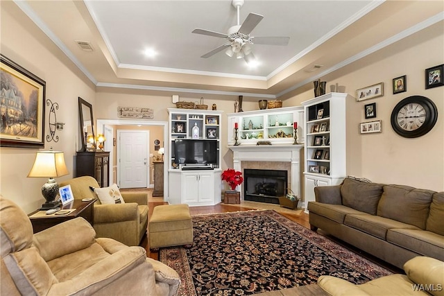 living room with wood-type flooring, a fireplace, ornamental molding, a raised ceiling, and ceiling fan