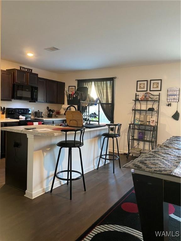 kitchen featuring a kitchen breakfast bar, dark brown cabinets, black appliances, and dark hardwood / wood-style floors