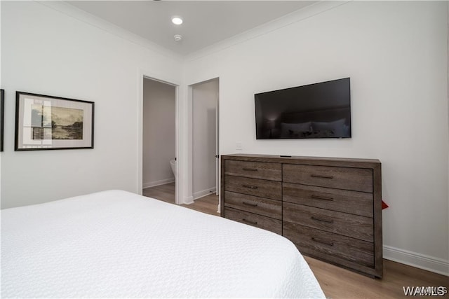 bedroom with hardwood / wood-style flooring, connected bathroom, and crown molding