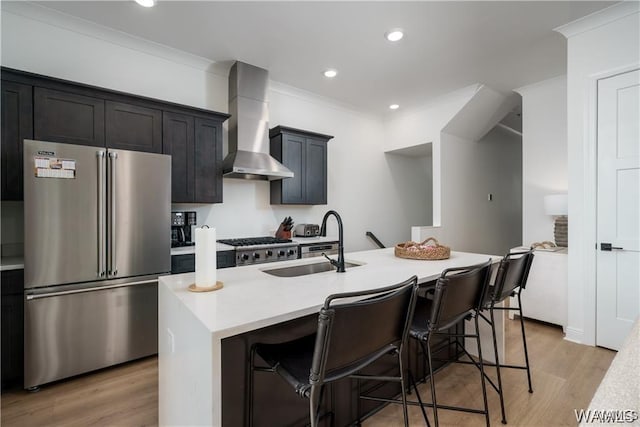 kitchen featuring a kitchen island with sink, a kitchen breakfast bar, sink, stainless steel appliances, and wall chimney exhaust hood