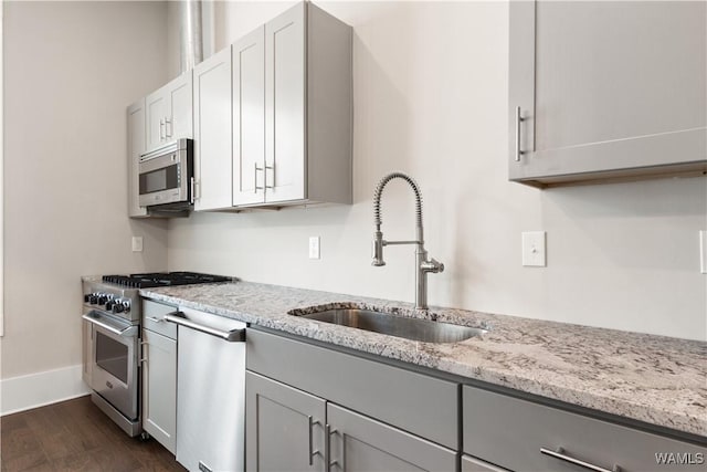 kitchen with light stone counters, stainless steel appliances, gray cabinets, dark wood-type flooring, and a sink