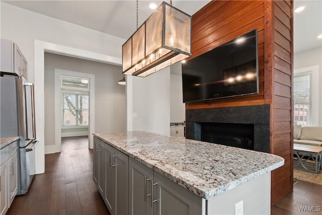 kitchen with dark wood-style floors, a fireplace, gray cabinetry, freestanding refrigerator, and light stone countertops