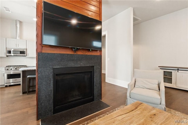 interior space featuring visible vents, appliances with stainless steel finishes, a fireplace with flush hearth, white cabinetry, and wood finished floors