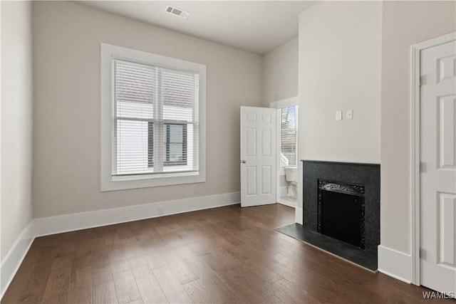 unfurnished living room with dark wood-style flooring, a fireplace with flush hearth, visible vents, and baseboards