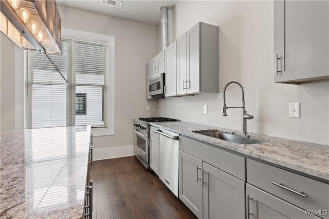 kitchen with light stone counters, stainless steel appliances, a sink, baseboards, and dark wood-style floors