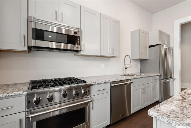 kitchen featuring stainless steel appliances, dark wood finished floors, a sink, and light stone counters