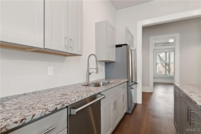 kitchen featuring baseboards, dark wood-style floors, appliances with stainless steel finishes, light stone counters, and a sink