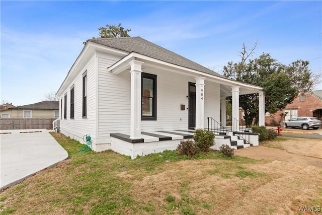 view of front of house with a shingled roof, covered porch, fence, a patio area, and a front yard