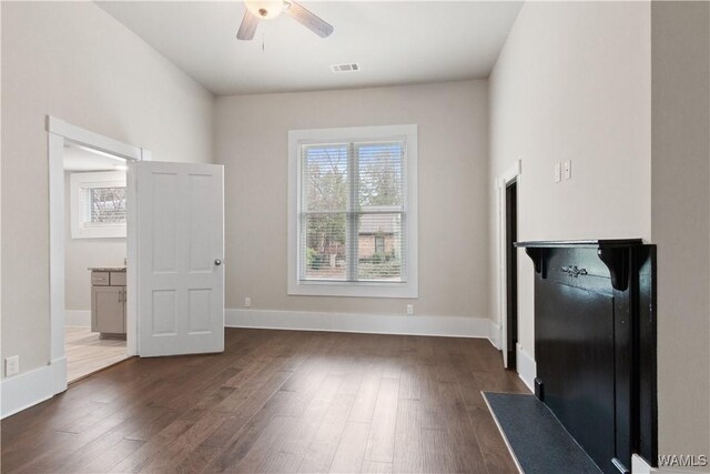 interior space featuring dark wood-style flooring, visible vents, ceiling fan, and baseboards