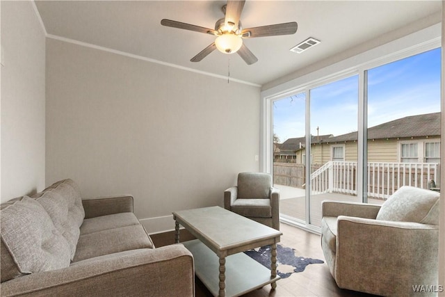 living area featuring ceiling fan, wood finished floors, visible vents, baseboards, and ornamental molding