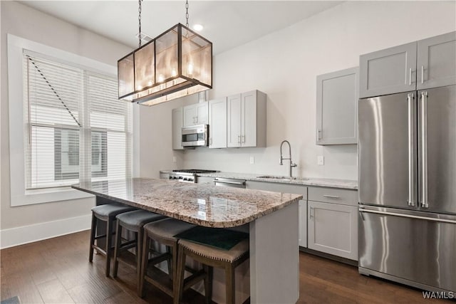 kitchen with appliances with stainless steel finishes, a breakfast bar, a center island, gray cabinets, and a sink