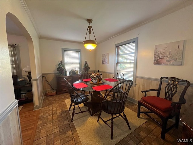 dining room with arched walkways, crown molding, wainscoting, and a healthy amount of sunlight