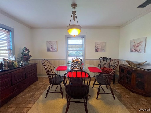 dining room featuring a wainscoted wall, ornamental molding, wood walls, and visible vents