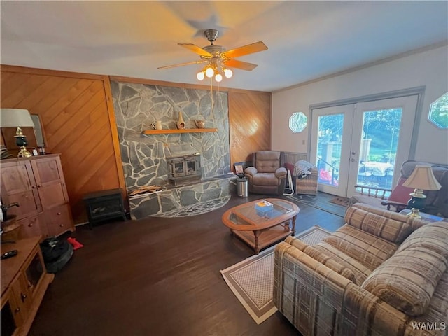 living area featuring dark wood-style floors, french doors, a ceiling fan, a wood stove, and wooden walls