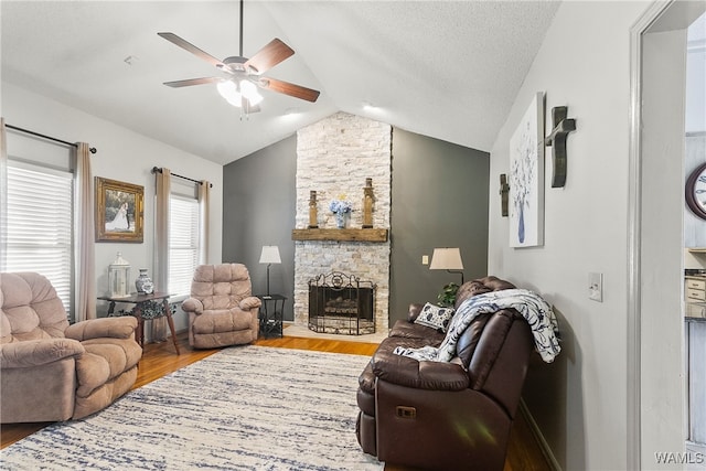 living room featuring lofted ceiling, a stone fireplace, hardwood / wood-style flooring, ceiling fan, and a textured ceiling