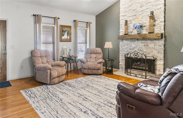 living room with wood-type flooring, vaulted ceiling, and a stone fireplace