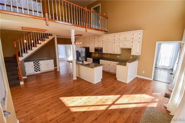 kitchen featuring white cabinets, appliances with stainless steel finishes, a towering ceiling, an island with sink, and sink