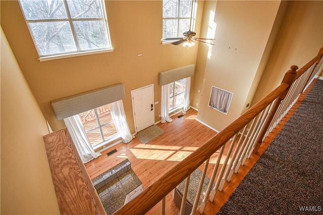 stairway featuring ceiling fan, a healthy amount of sunlight, wood-type flooring, and a high ceiling